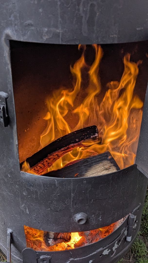 Helle orangefarbene Flammen lodern aus dem offenen oberen Teil eines schwarzen Holzofens, während unten glühende Kohlen zu sehen sind.   Quellen und ähnliche Inhalte